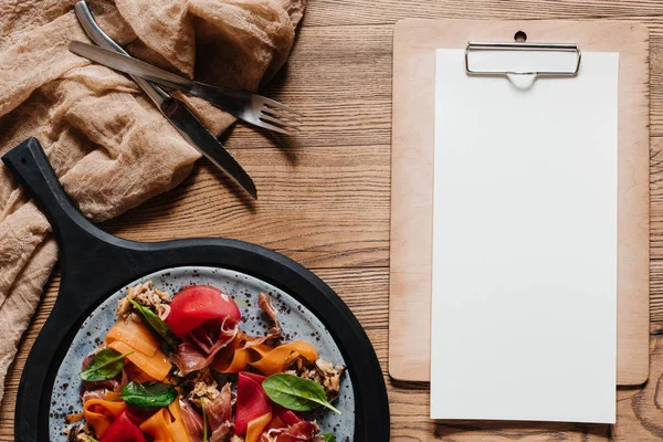 Insalata con cozze, verdure e marmellata, forchetta con coltello e carta bianca sugli appunti sul tavolo di legno — Foto stock