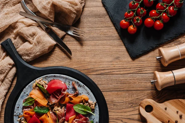 Ensalada con mejillones, verduras y jamón, tenedor con cuchillo y tomates frescos sobre mesa de madera - foto de stock