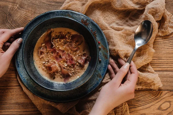Cropped shot of person holding spoon and eating delicious cream soup with jamon — Stock Photo