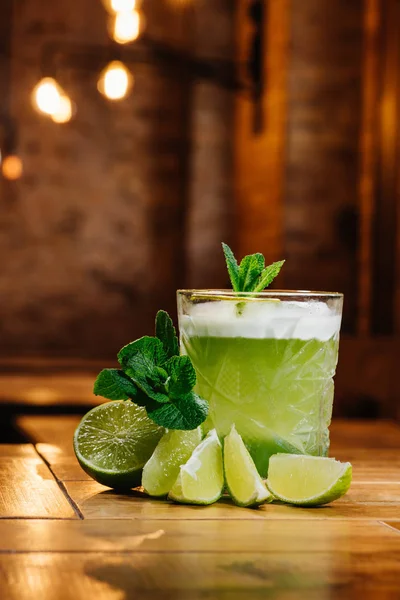 Крупним планом зелений коктейль для окулярів у склянці з м'ятою та лаймом на дерев'яному столі — стокове фото