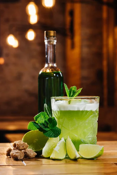 Close-up view of green van gogh cocktail in glass with bottle of absinthe on wooden table — Stock Photo