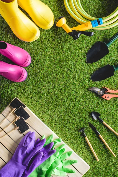 Vista superior de pizarras vacías, botas de goma, guantes de protección y equipo de jardinería en la hierba - foto de stock