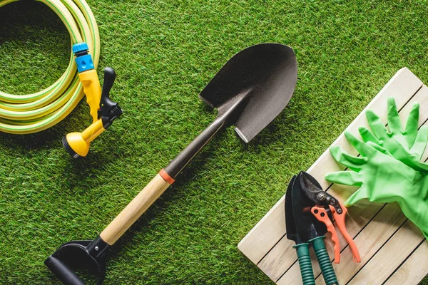 Schlauchleitung, Schutzhandschuhe und Gartengeräte im Gras von oben — Stockfoto