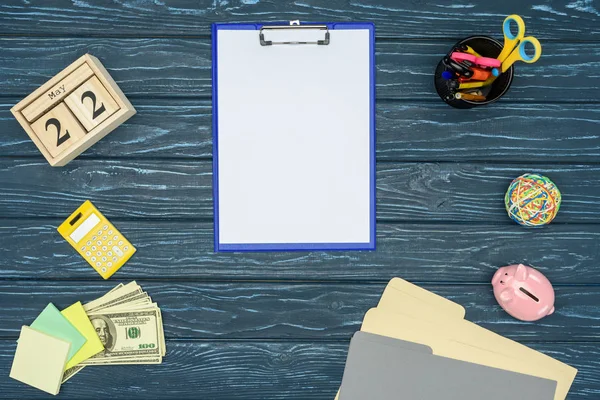 Clipboard with blank paper on blue wooden table with stationery and money — Stock Photo