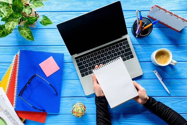 Close-up view of notepads in hands by laptop on blue wooden table — Stock Photo