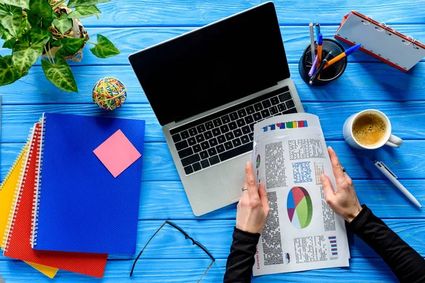 Geschäftsmann hält Charts per Laptop auf blauem Holztisch mit Schreibwaren — Stockfoto