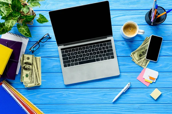 Open laptop on blue wooden table with stationery and money — Stock Photo