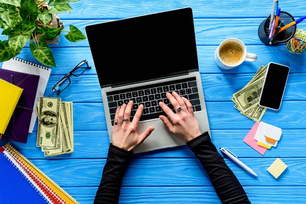 Mãos digitando no teclado do laptop na mesa de madeira azul com artigos de papelaria e dinheiro — Fotografia de Stock