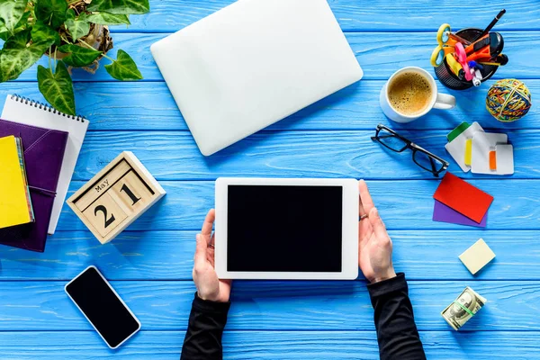 Mains tenant tablette sur table en bois bleu avec de l'argent et de la papeterie — Photo de stock