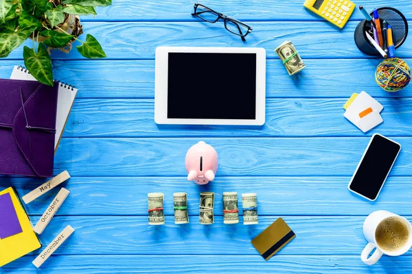 Цифровой планшет с копилкой и деньгами на синем деревянном столе — стоковое фото