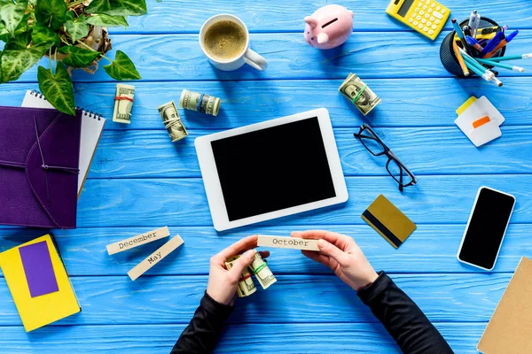 Vista de cerca de las manos sosteniendo el calendario y el dinero en la mesa de madera azul con la tableta - foto de stock