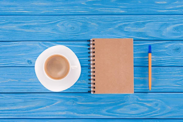 Top view of coffee cup, textbook and pen on blue wooden planks — Stock Photo