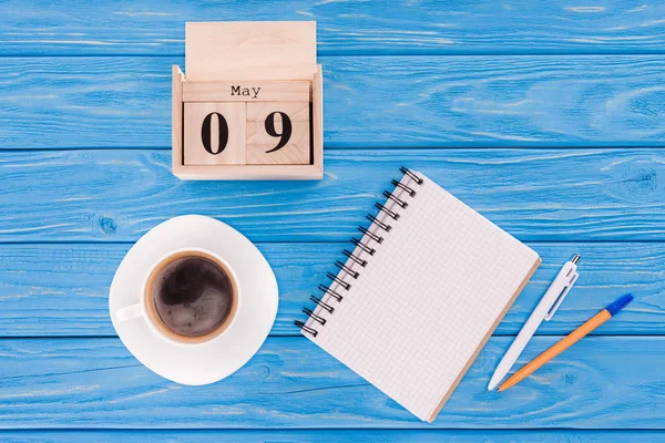 Vista superior do calendário de madeira com data de 9 de maio, xícara de café, livro didático em branco e canetas, conceito de dia de vitória — Fotografia de Stock