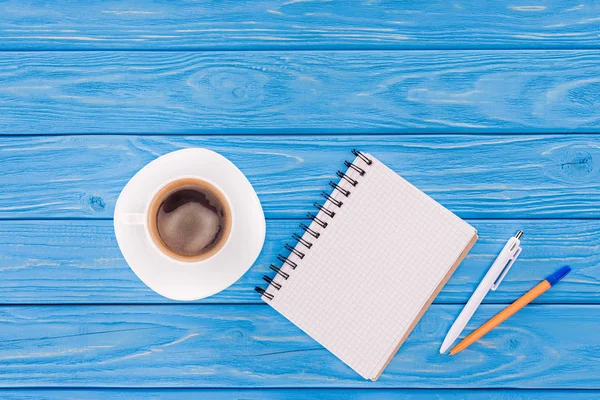 Blick von oben auf leeres Lehrbuch, Kugelschreiber und Kaffeetasse auf blauen Holzplanken — Stockfoto