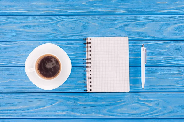 Vista superior de libro de texto vacío, pluma y taza de café en tablones de madera azul - foto de stock