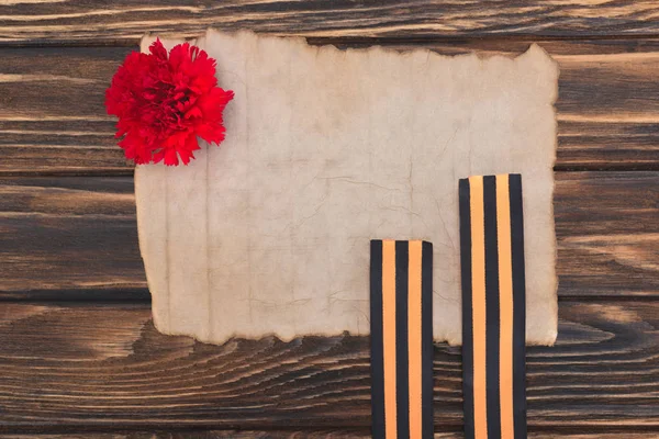 Верхний вид старой пустой бумаги, гвоздики и ленты св. Георгия на деревянной поверхности — стоковое фото