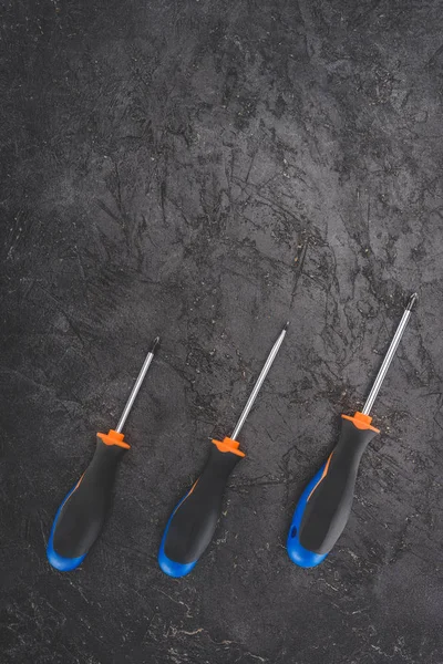 Top view of three screwdrivers placed in row on black rustic surface — Stock Photo