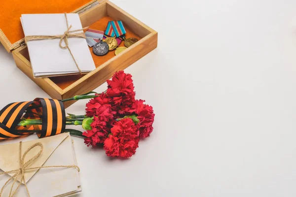 Closeup shot of box with medals, stacks of letters, carnations wrapped by st. george ribbon on gray, victory day concept — Stock Photo