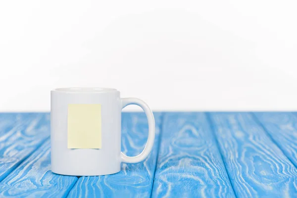 Primer plano de la taza con papel de nota vacío en la superficie azul de madera - foto de stock