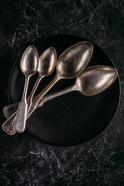 Black plate and vintage spoons on dark background — Stock Photo