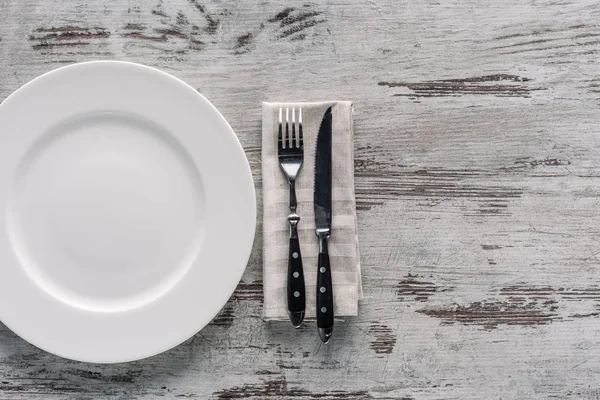 Piatto bianco e forchetta con coltello su tovagliolo su tavolo di legno — Foto stock