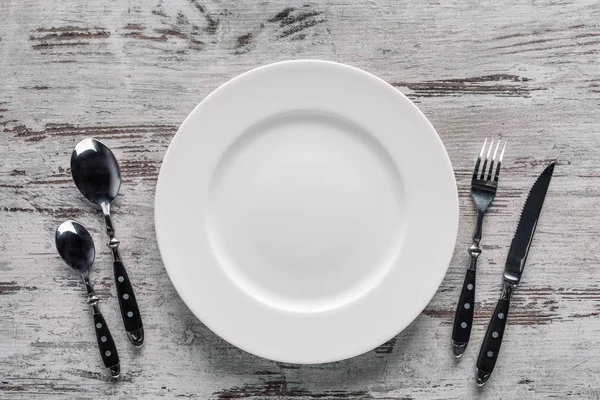 Белая тарелка и столовое серебро на деревенском деревянном фоне — стоковое фото