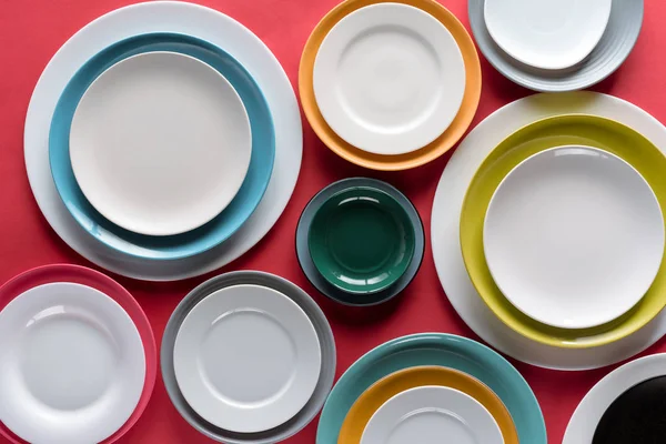 White and colorful plates of different sizes on red background — Stock Photo