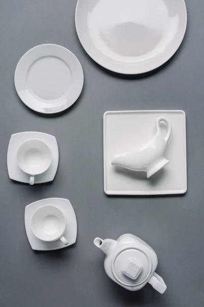 Білі тарілки з чайником і чашками на сірому фоні — стокове фото