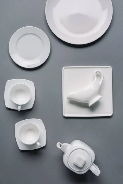 Platos blancos con tetera y tazas sobre fondo gris - foto de stock