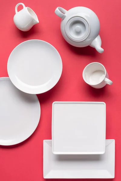 Assiettes de vaisselle blanches et ensemble de thé sur fond rouge — Photo de stock