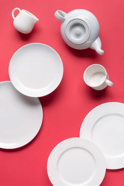 Platos blancos con tetera y taza sobre fondo rojo - foto de stock