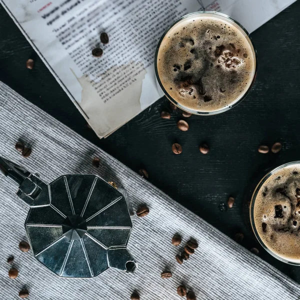 Flat lay com cafeteira, jornal e copos de café frio em mesa preta — Fotografia de Stock