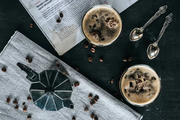 Tumbado plano con cafetera, cucharas, periódico y vasos de café elaborado en frío sobre una mesa negra - foto de stock