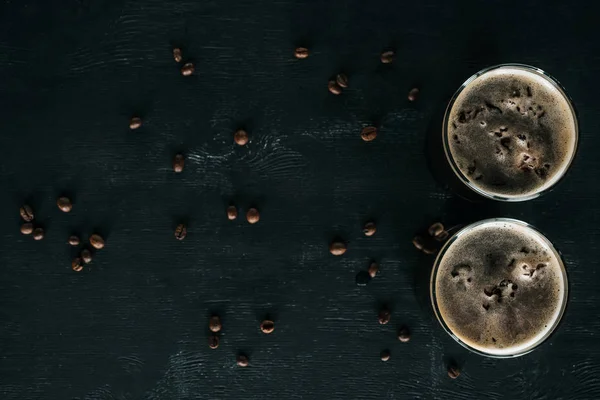 Vista superior de vasos de café elaborado en frío con hielo en la superficie oscura con granos de café tostados alrededor - foto de stock