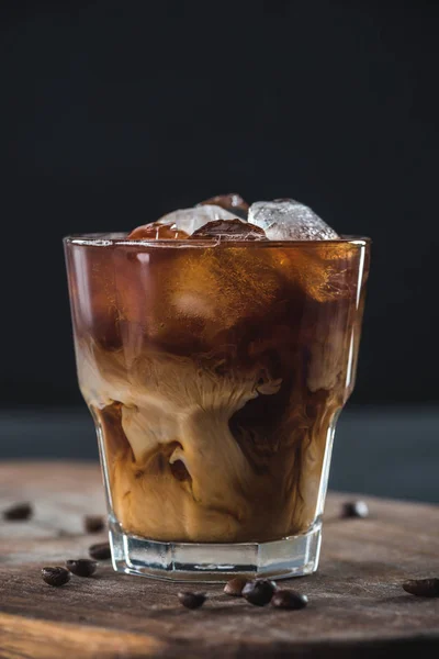 Close up view of glass of cold brewed coffee with roasted coffee beans on wooden cutting board on dark backdrop — Stock Photo