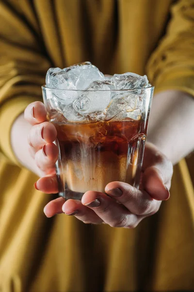 Partial view of woman holding glass of cold brewed coffee with ice cubes in hands — Stock Photo