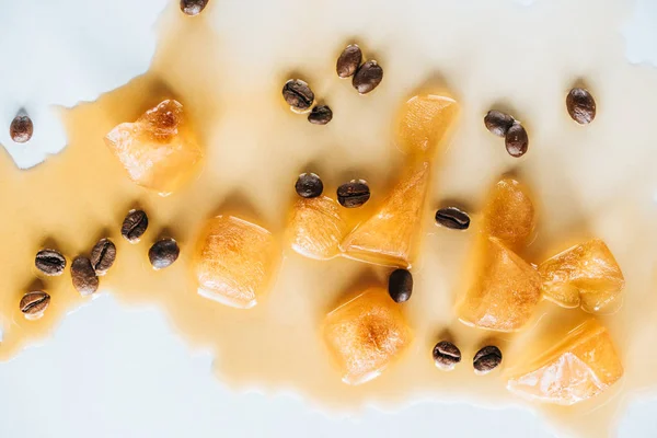 Vista dall'alto di cubetti di ghiaccio marrone fatti di caffè e chicchi di caffè tostati su un tavolo bianco — Foto stock
