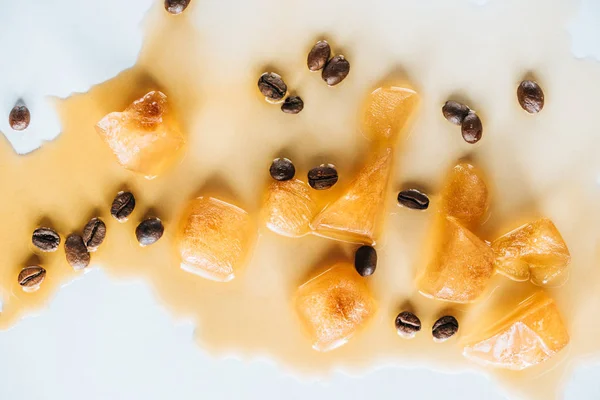 Vista superior de cubitos de hielo marrón hechos de café y granos de café tostados en la mesa blanca - foto de stock