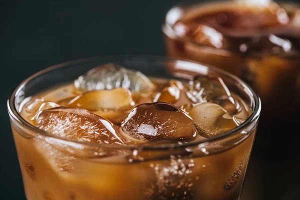 Close up view of ice cubes in cold brewed coffee in glass on dark background — Stock Photo