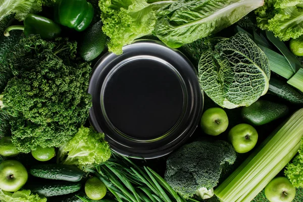 Top view of black plate between green vegetables, healthy eating concept — Stock Photo