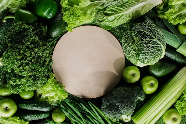 Vista superior da placa de madeira redonda entre vegetais verdes, conceito de alimentação saudável — Fotografia de Stock