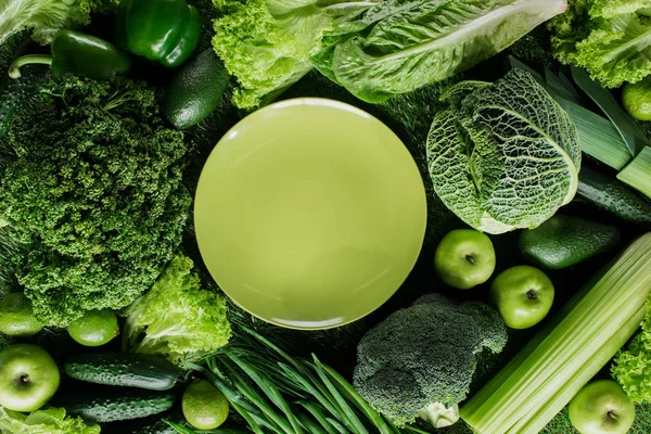 Top view of green plate between green vegetables, healthy eating concept — Stock Photo