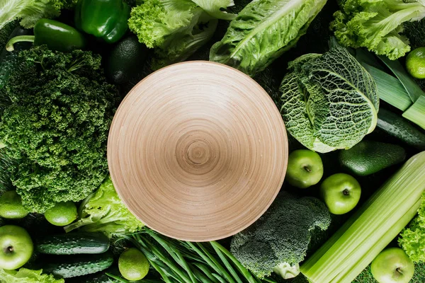 Top view of round cutting board between green vegetables, healthy eating concept — Stock Photo