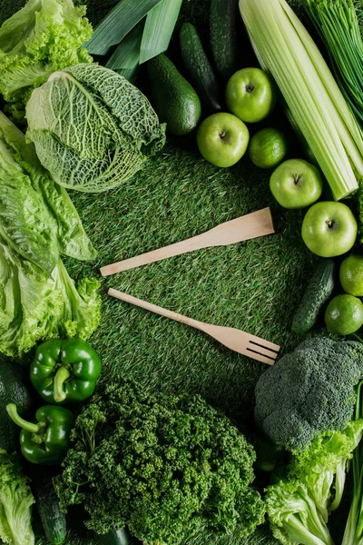 Верхний вид деревянной лопатки и вилки между зелеными овощами, концепция здорового питания — стоковое фото