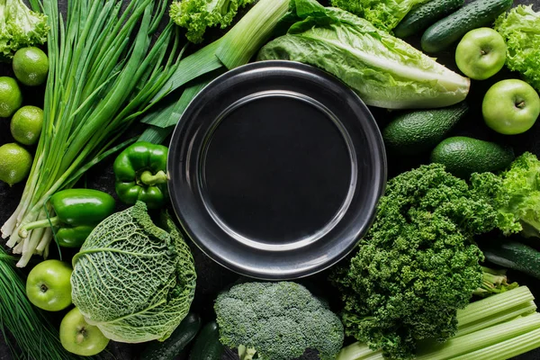 Top view of black plate between green vegetables, healthy eating concept — Stock Photo