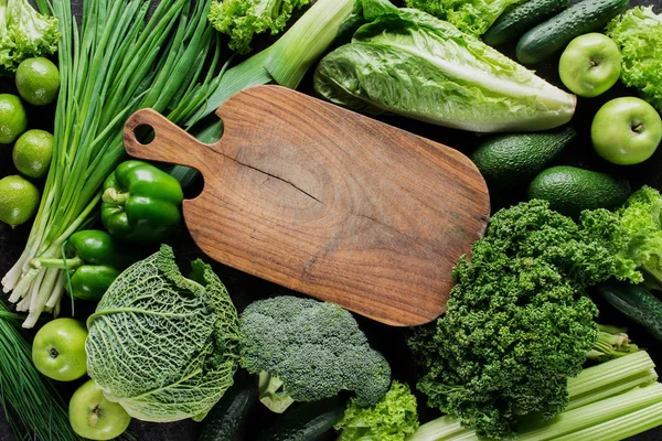 Vista superior de tablero de madera entre verduras verdes, concepto de alimentación saludable - foto de stock