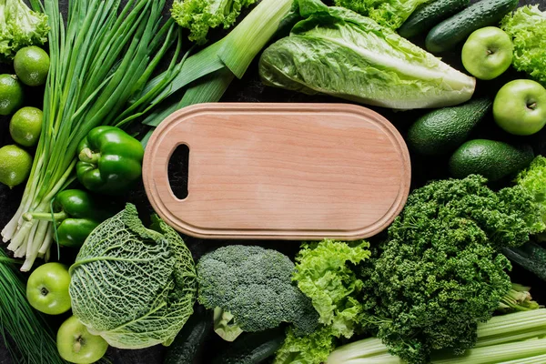 Top view of cutting board between green vegetables, healthy eating concept — Stock Photo