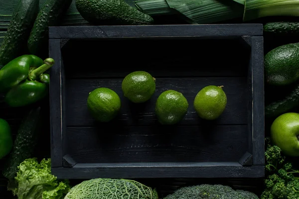 Top view of lime in wooden box between green vegetables, healthy eating concept — Stock Photo