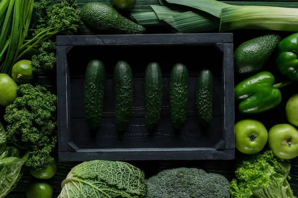 Vista superior de pepinos em caixa de madeira entre vegetais verdes, conceito de alimentação saudável — Fotografia de Stock