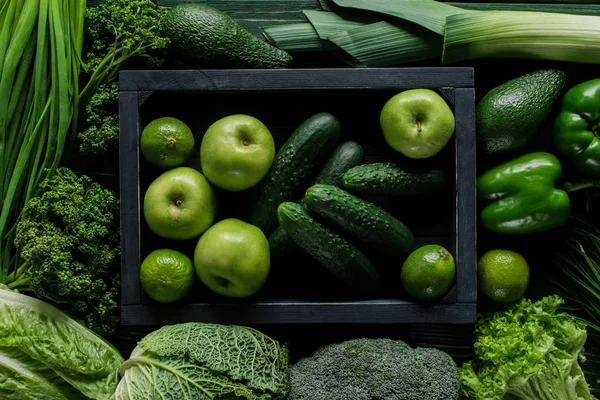 Vista superior de manzanas y pepinos en caja de madera entre verduras verdes, concepto de alimentación saludable - foto de stock